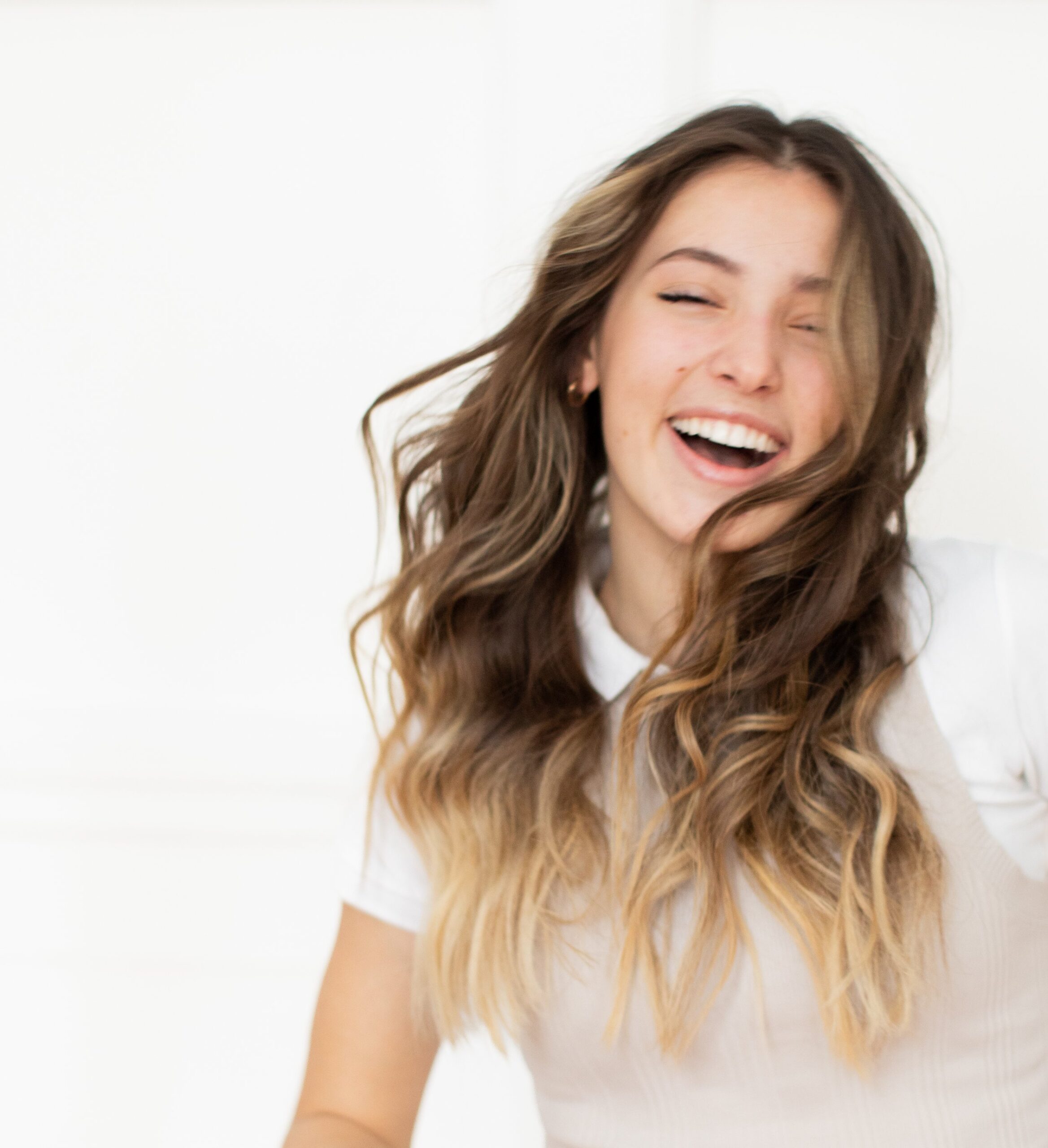 Jayden Campbell Photography. Photo of a teen girl laughing in front of a white wall in neutral colours in Calgary Alberta Canada